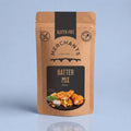 A stand-up kraft paper pouch of Merchant's Batter Mix, 250g, featuring a black and brown label with a food photo of battered fish and chips, set against a light blue background.