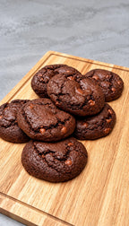 A pile of chocolate chip cookies on a wooden cutting board against a gray textured background.