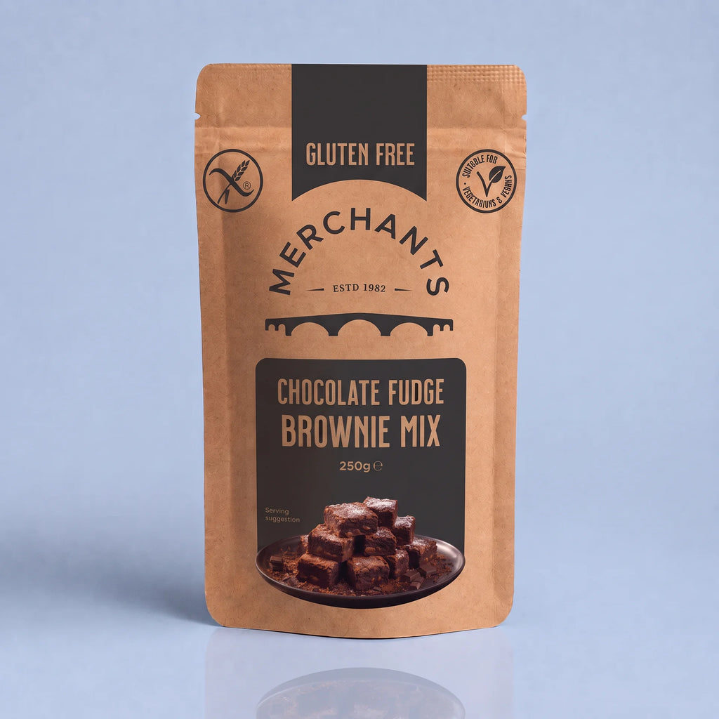 A stand-up pouch of Merchants Chocolate Fudge Brownie Mix, 250g, on a light blue-gray background with a soft reflection below. The packaging is a warm kraft brown with dark brown panels and text, featuring a photo of chocolate brownies on the front.
