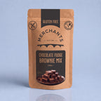 A stand-up pouch of Merchants Chocolate Fudge Brownie Mix, 250g, on a light blue-gray background with a soft reflection below. The packaging is a warm kraft brown with dark brown panels and text, featuring a photo of chocolate brownies on the front.
