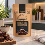 A stand-up kraft paper pouch of Merchants Chocolate Fudge Brownie Mix stands on a kitchen countertop, with brownies and baking props visible in a real kitchen setting.