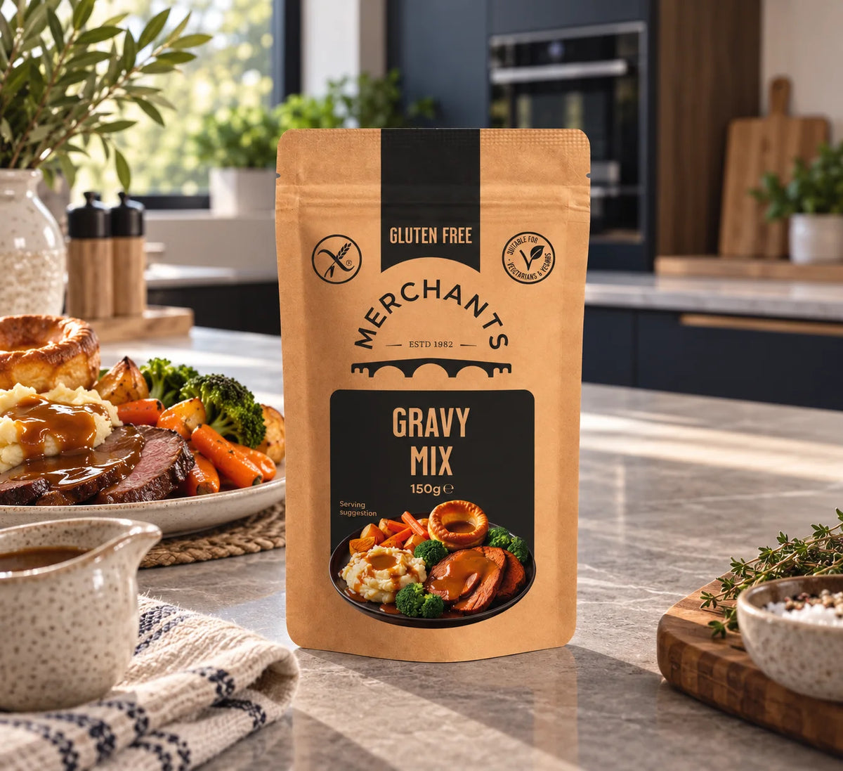 A stand-up pouch of Merchants Gluten Free Gravy Mix stands on a kitchen countertop, with plated cooked meat, potatoes, carrots, and broccoli in the background. The package is kraft paper with black panels and a food photo on the front.