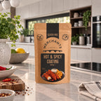 A stand-up pouch of Merchants Gluten Free Hot & Spicy Coating stands on a kitchen countertop. The kraft paper bag has a black label with white and gold text and a photo of coated food on the front.