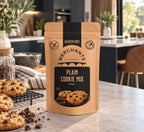 A stand-up pouch of Merchants Gluten Free Plain Cookie Mix, 250g, displayed on a kitchen countertop with cookies and chocolate pieces in the foreground.